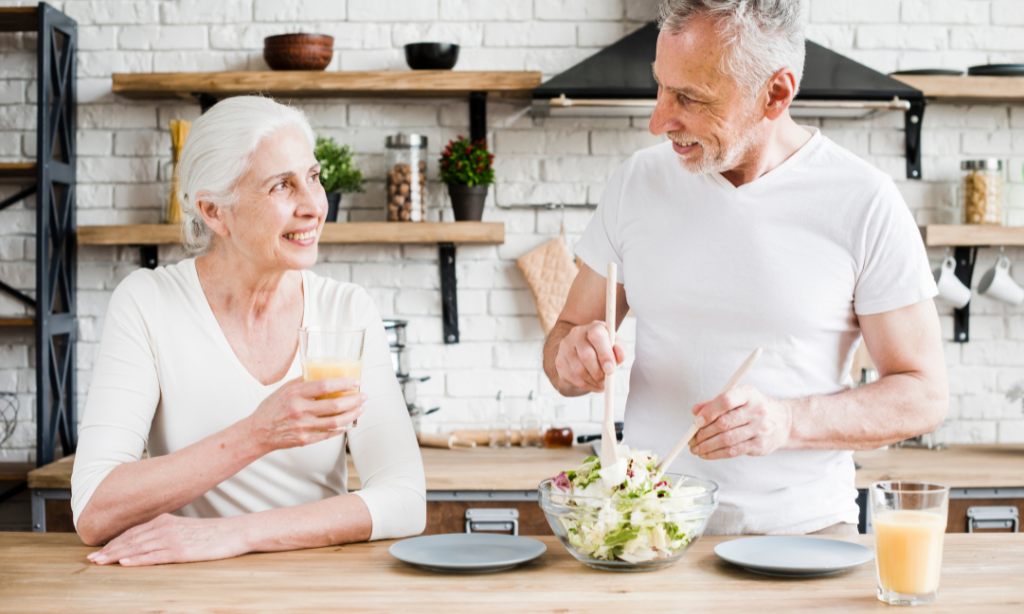 An older couple preparing and enjoying a healthy meal together in the kitchen, representing balanced nutrition and healthy ageing.