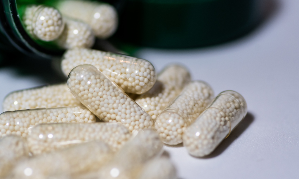 Close-up of transparent nattokinase capsules filled with white granules spilling from a container, representing high-quality nattokinase supplements UK for heart health and circulation support.