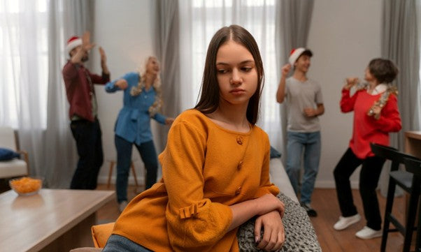 A person sits on a sofa looking upset while others socialize in the background, illustrating anxiety, low mood, and mental overwhelm associated with gut brain health.