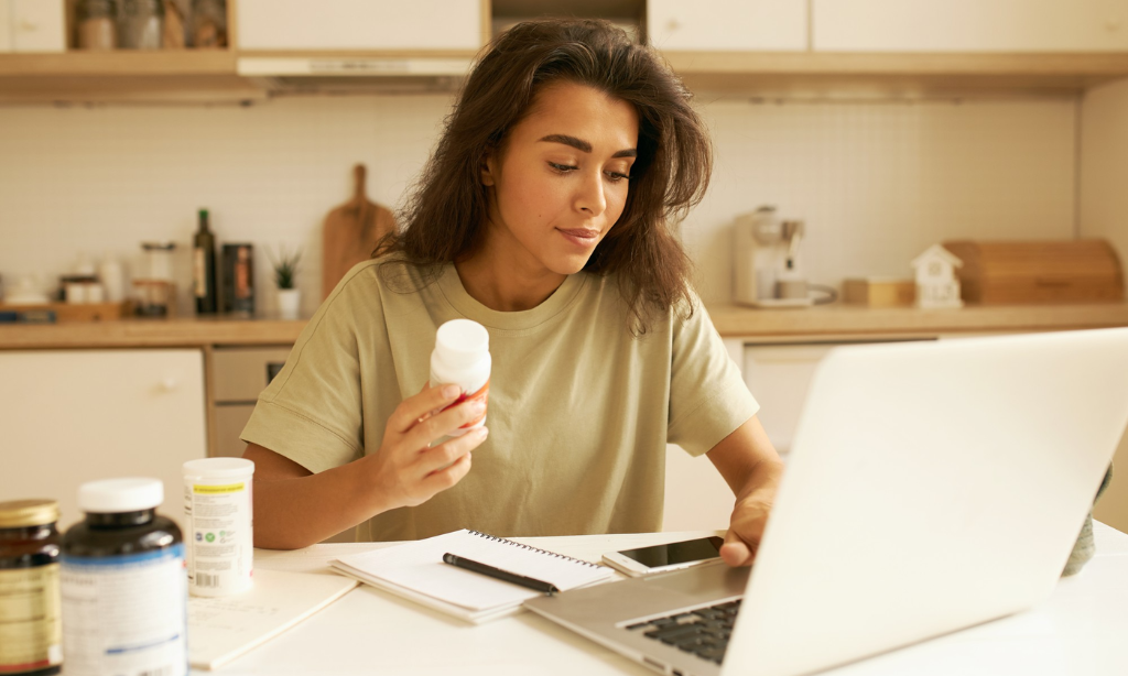 Woman researching nattokinase dosage and wellness supplements at home while using a laptop in a modern kitchen setting.