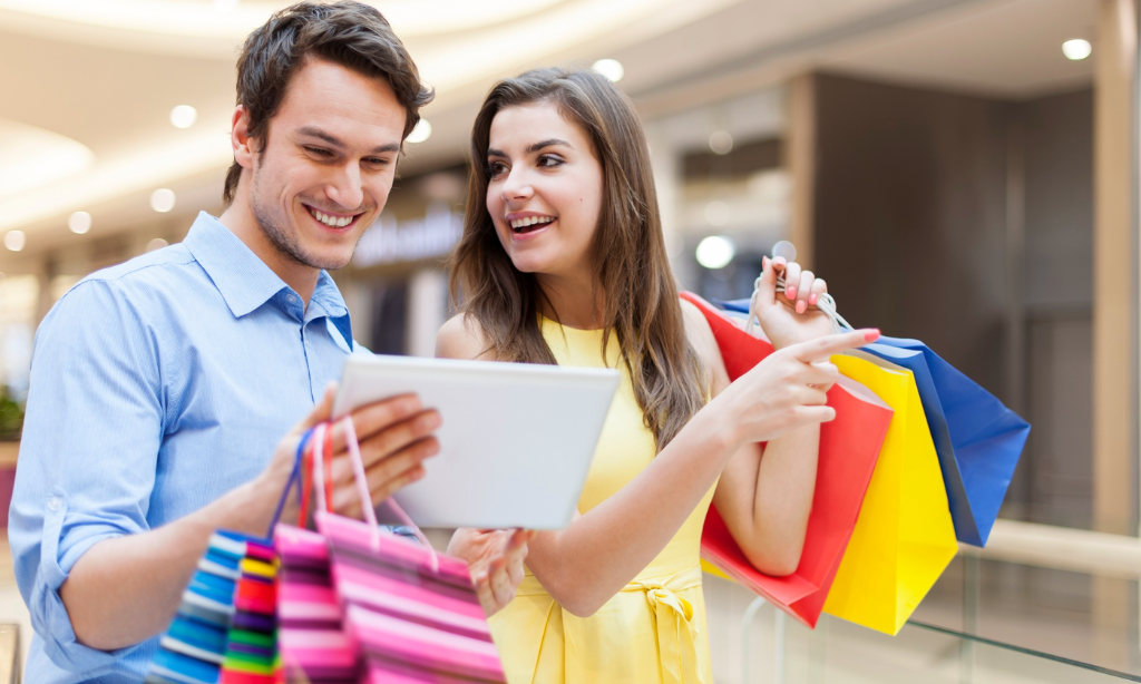 Happy couple shopping together while looking at a tablet in a mall, representing smart buying decisions, product comparison, and customer shopping experience.