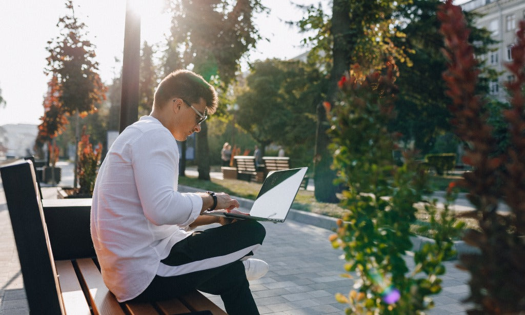A person sits on a bench outdoors, working on a laptop. This scene shows how modern lifestyle stress, screen time, and irregular meals can affect gut health.