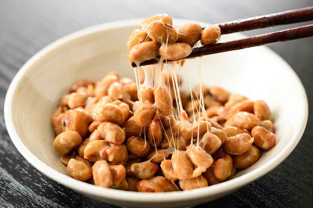 Bowl of Japanese natto with sticky fermented soybeans being picked up with chopsticks.