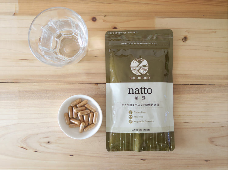 sonomono™ Natto powder capsules on a wooden table with a glass of water