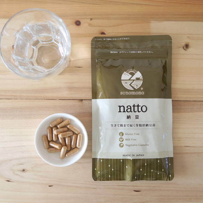 sonomono™ Natto powder capsules on a wooden table with a glass of water