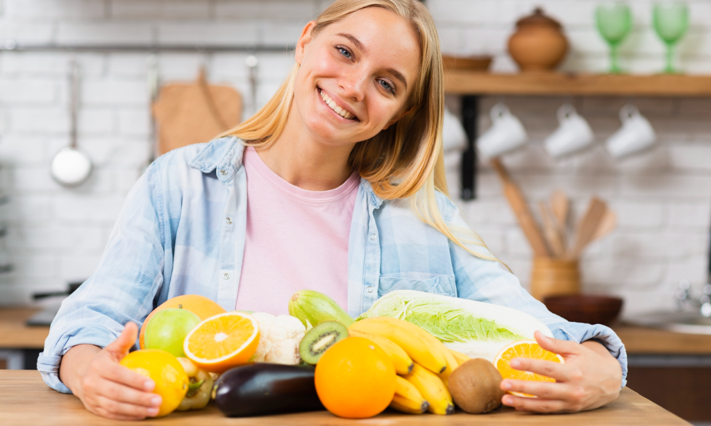 Smiling woman with fresh fruits and vegetables, showcasing natural Vitamin K2-rich foods that support bone, heart, and overall health.