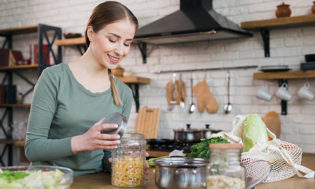 Woman preparing food in a home kitchen while storing ingredients in a glass jar, representing sustainable wellness habits, healthy meal preparation, and the role of fermented foods in everyday routines.
