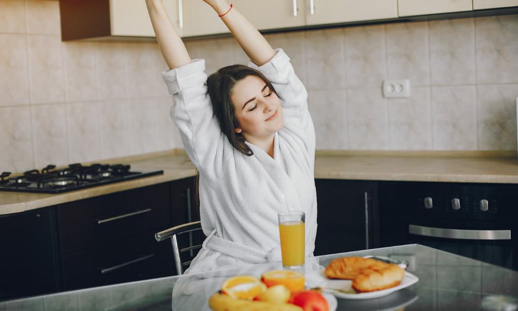 Woman stretching in her kitchen during breakfast, with fresh fruit, juice, and a healthy meal on the table, representing healthy circulation, daily wellness habits, and an active lifestyle.