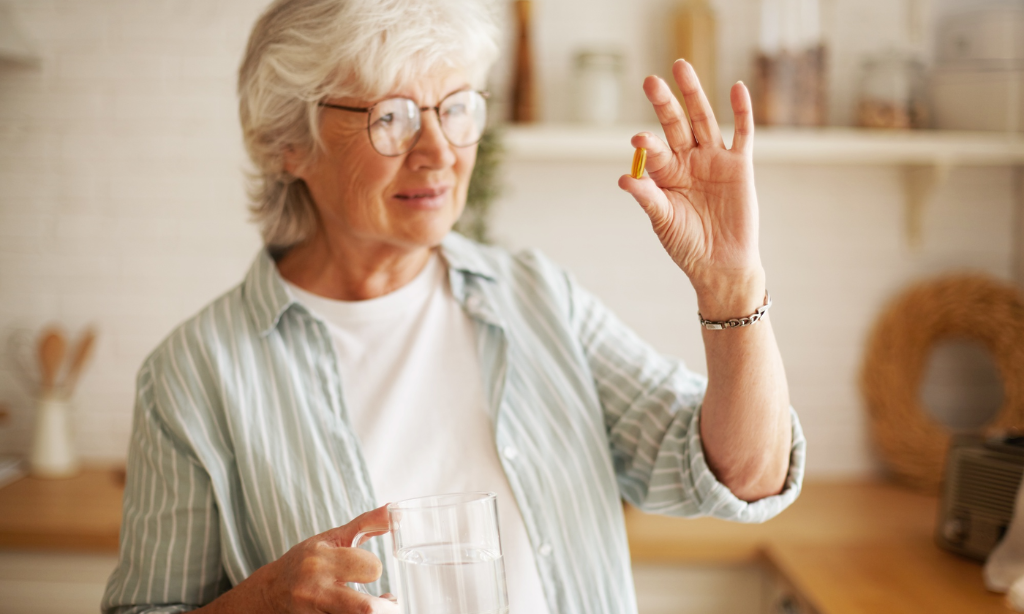 Older woman taking a daily wellness capsule with water as part of a simple and healthy supplement routine.