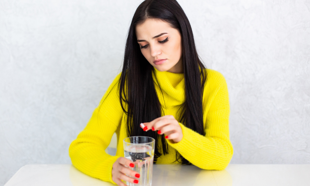 Woman holding a glass of water and taking a tablet, representing aspirin use or nattokinase capsules UK for blood clot support and heart health.