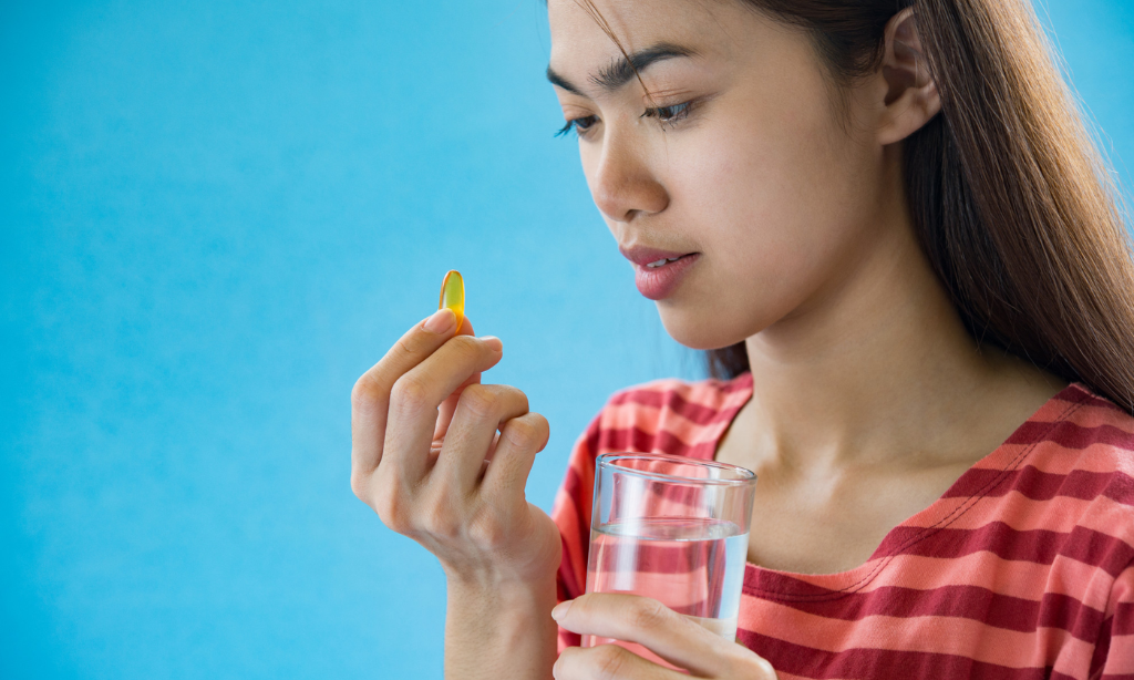 Woman taking Vitamin K2 supplement with water for bone health and wellness