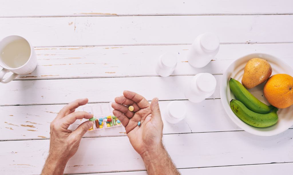 Person holding vitamin supplements beside fresh fruits, highlighting the role of vitamin K2 and calcium in bone health.