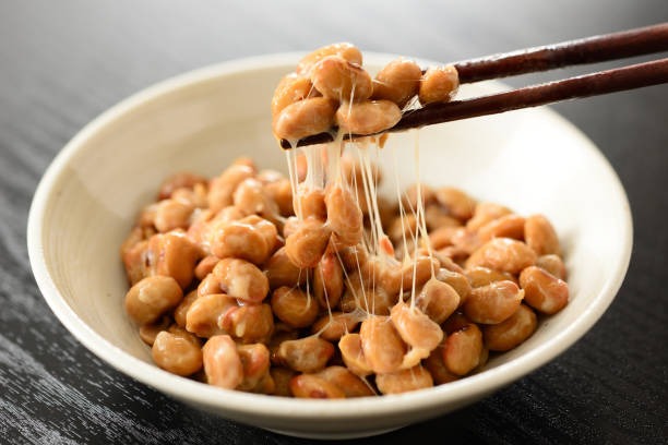 Sticky fermented soybeans (natto) being lifted with chopsticks over a bowl, highlighting traditional Japanese food known as a natural source of nattokinase.