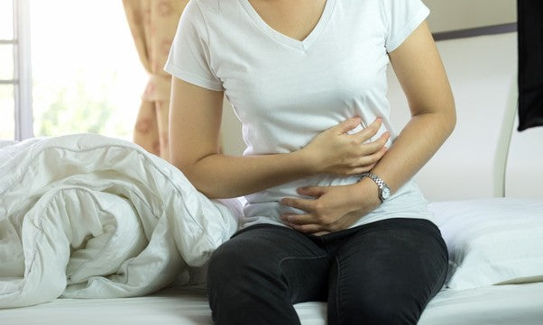 Person sitting on a bed holding their abdomen, showing stomach discomfort—illustrating gut sensitivity after antibiotics.